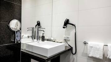 A modern bathroom with a white sink, two faucets, a hairdryer, and a towel rack.