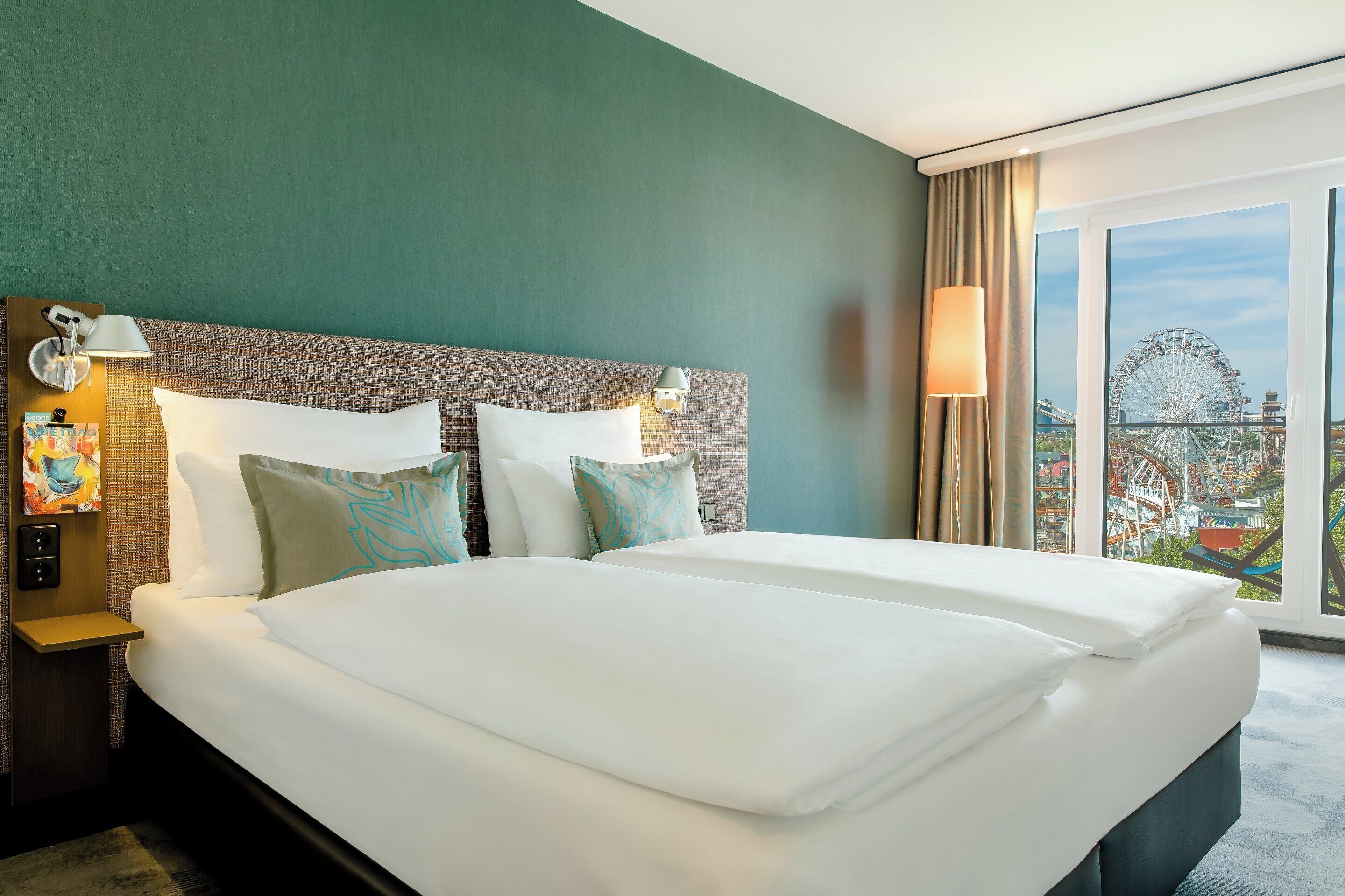 Ein Hotelzimmer mit einem großen Bett, zwei Nachttischlampen, einem Nachttisch und Blick auf ein Riesenrad.