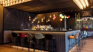 A bar area with a long counter, multiple stools, and a variety of bottles. - Motel One Wien-Prater (Vienna)
