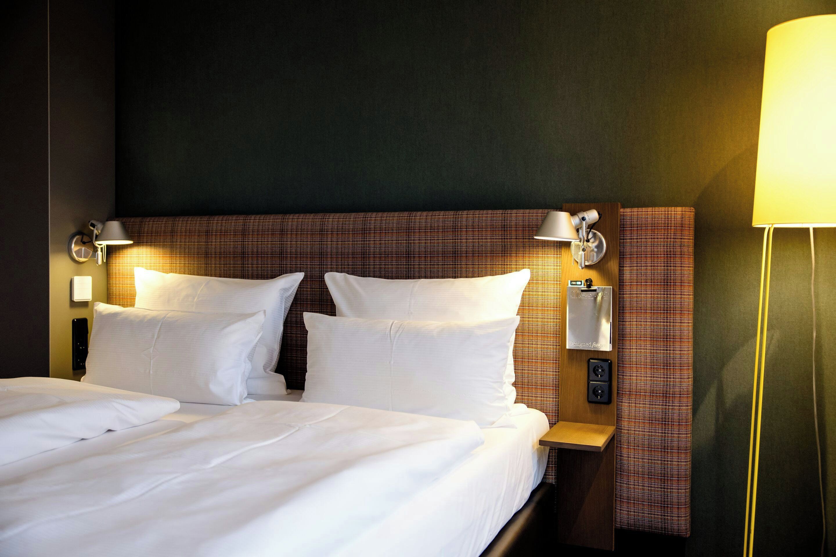 Ein Hotelzimmer mit einem großen Bett, zwei Nachttischen, einem Kopfteil und einer Wandlampe.
