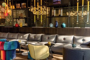 A modern interior with a sectional sofa, colorful chairs, and a variety of decorative items on shelves. - Motel One Wien-Prater (Vienna)