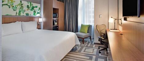 Habitación de hotel con una cama grande, un escritorio con silla, un televisor y un cuadro en la pared.