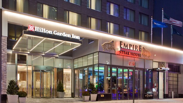 The exterior of the Hilton Garden Inn and Empire Steak House, featuring a glass facade and illuminated signage. - Hilton Garden Inn New York/Central Park South-Midtown West (New York)