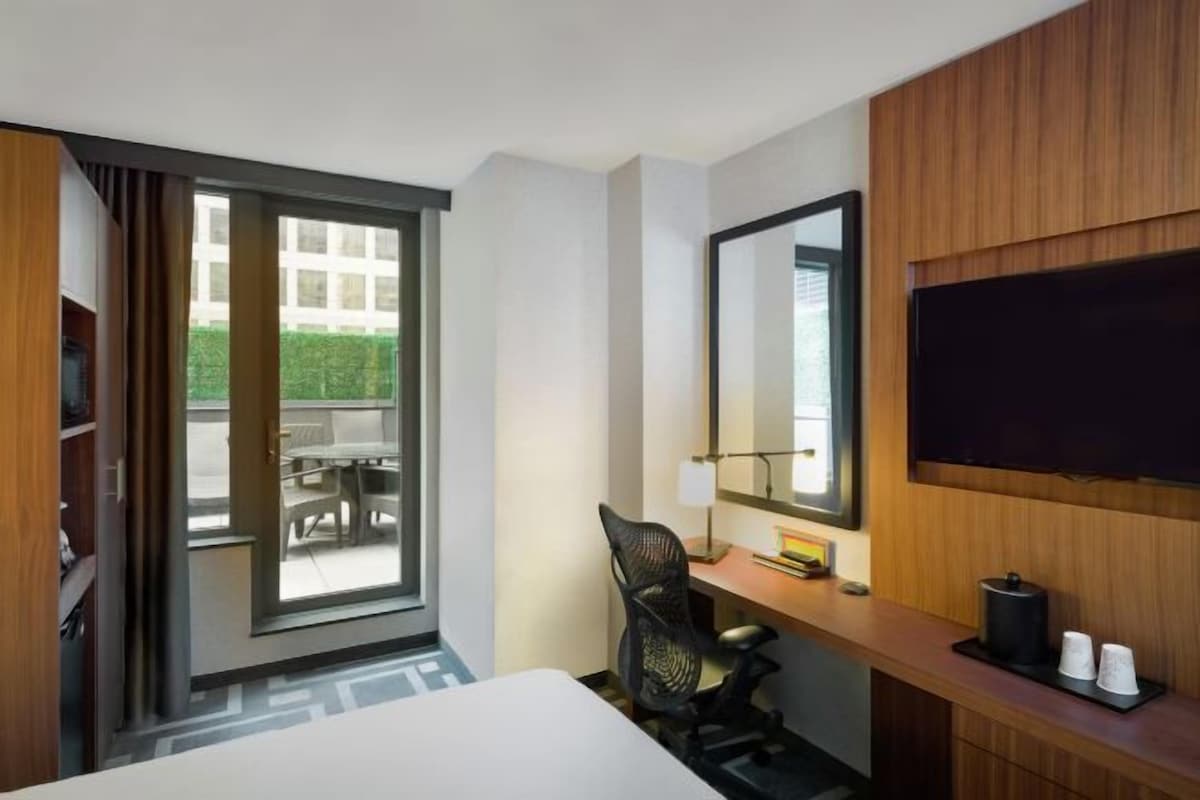 Ein Hotelzimmer mit Bett, Schreibtisch mit Stuhl, Fernseher und einem großen Fenster mit Blick ins Freie.