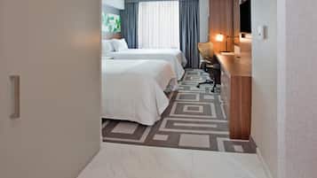 A hotel room with two beds, a desk, a chair, a TV, and a window with curtains.