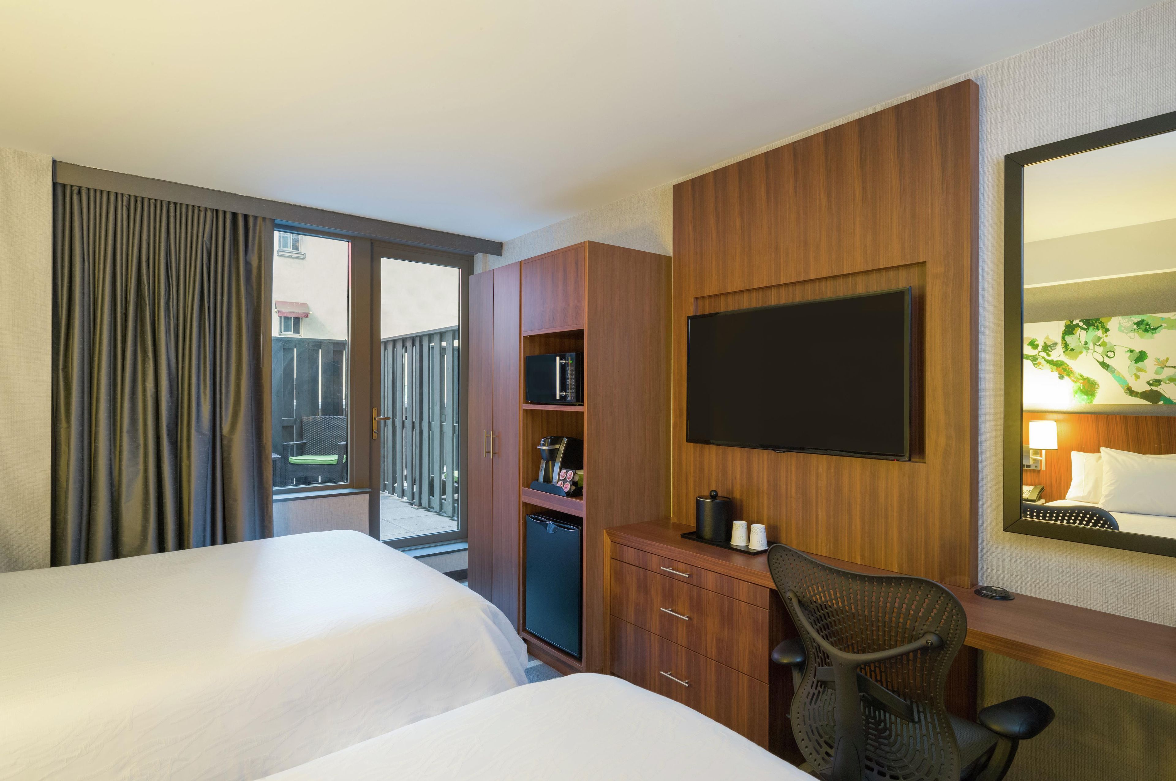 A hotel room with a bed, a desk with a chair, a television, and a minibar.