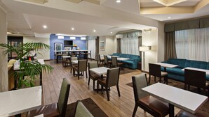 A hotel lobby with a dining area, sofas, and a kitchen in the background. - Hampton Inn Los Angeles Int'l Airport/Hawthorne (Hawthorne)