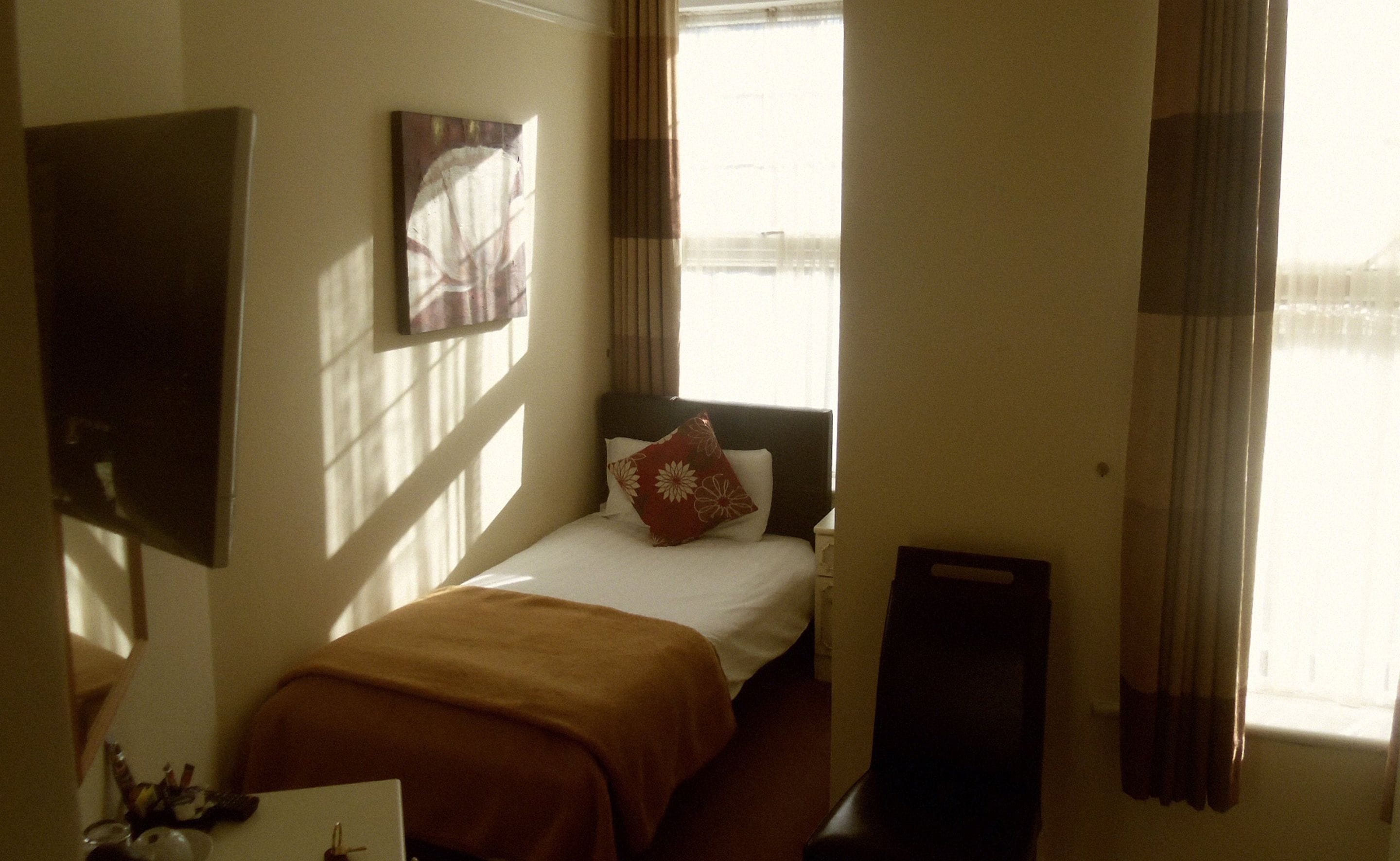A hotel room with a bed, a TV on the wall, and a window with curtains.