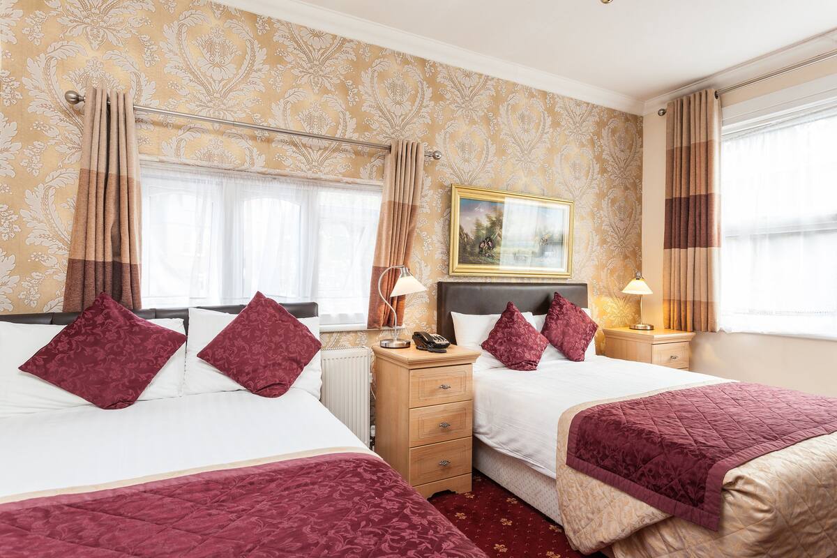 A hotel room with two beds, a nightstand, a lamp, and a painting on the wall.