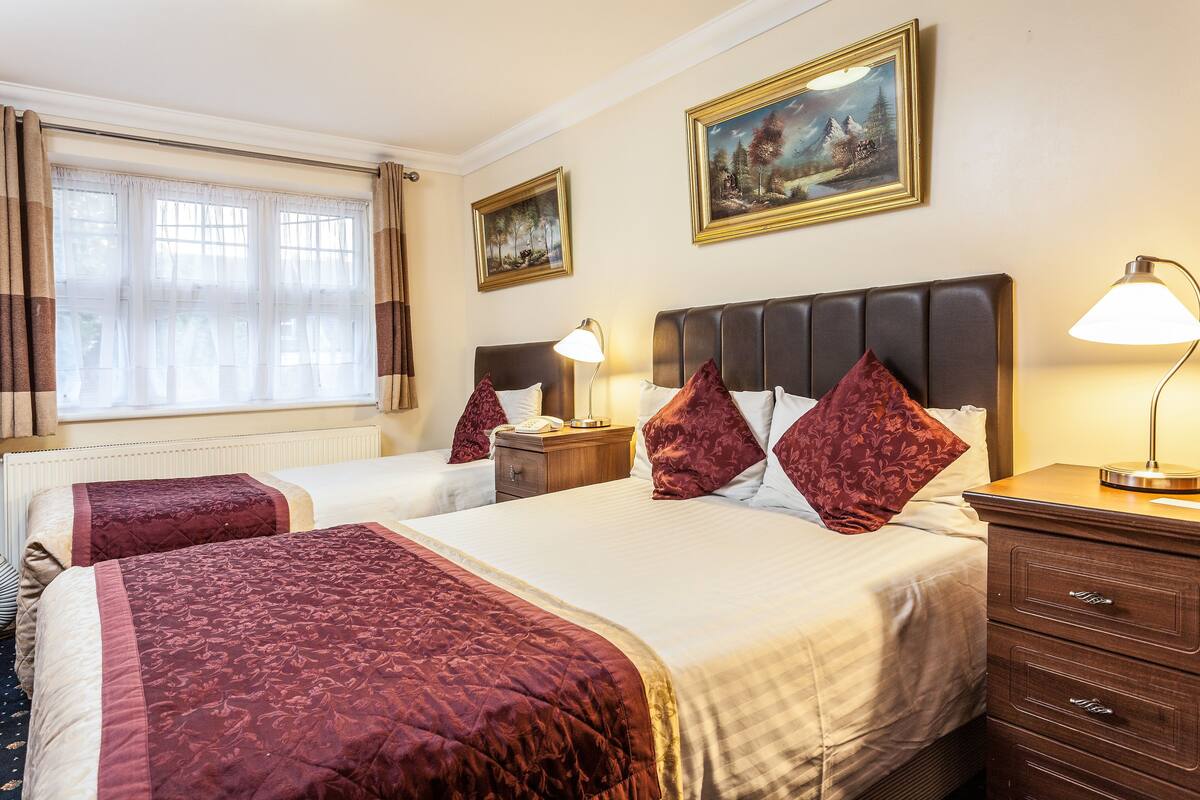 A hotel room with two beds, a nightstand, a lamp, and a painting on the wall.