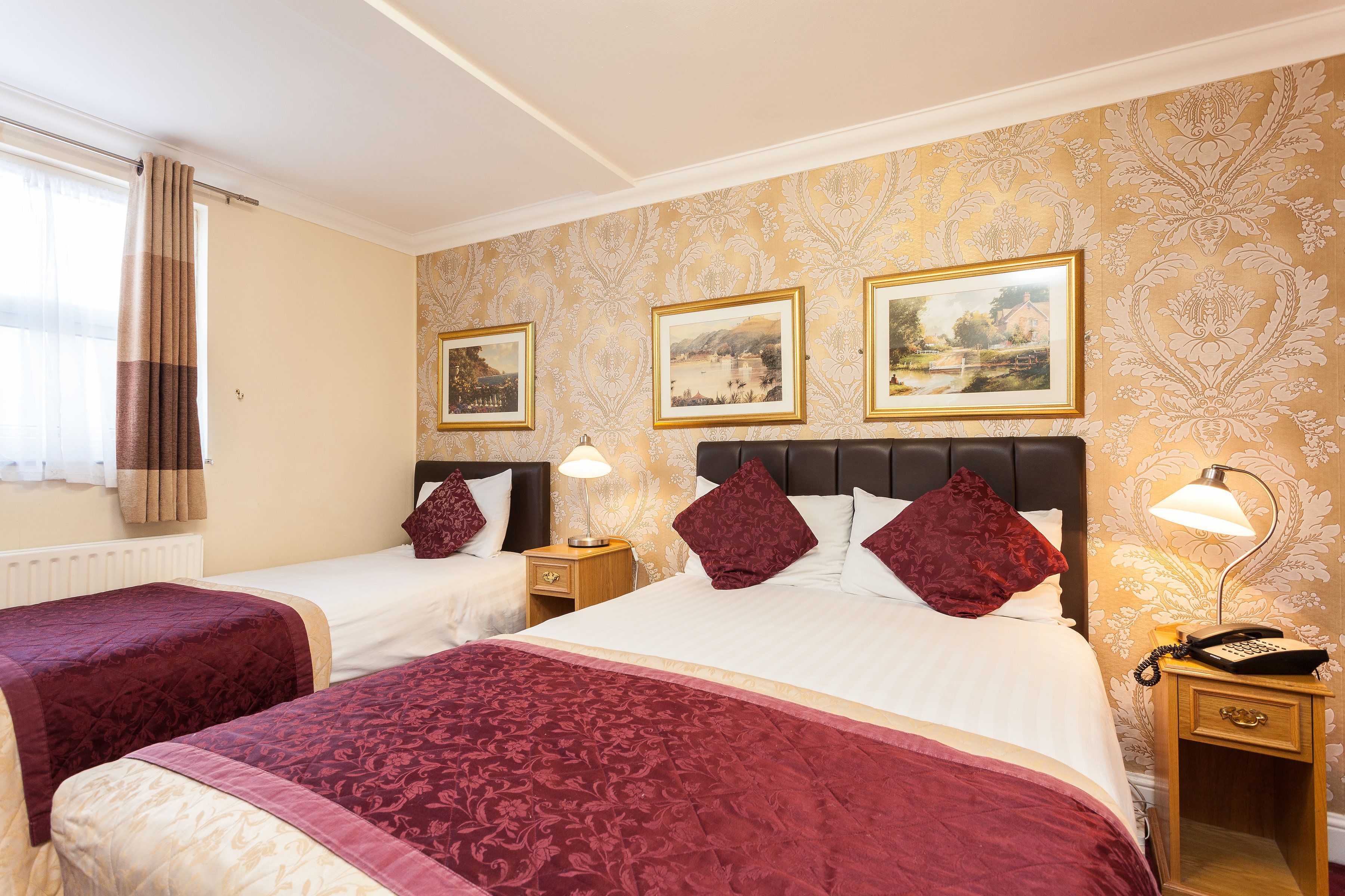 Une chambre d’hôtel avec deux lits, une table de chevet avec une lampe et trois tableaux encadrés au mur.