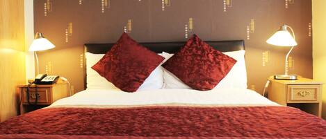 A neatly made bed with a red blanket and two red pillows, a bedside lamp, and a telephone on a wooden nightstand.