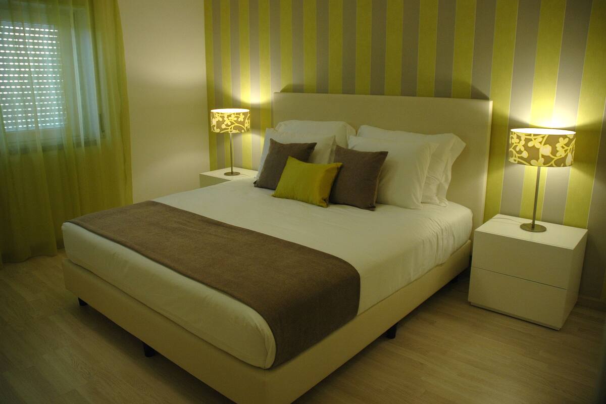 Una cama bien hecha con una manta marrón, dos lámparas de noche y una pared a rayas en una habitación de hotel.