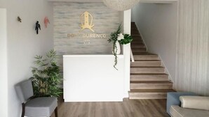 Et hotellets receptionområde med moderne design, med en receptionsdisk, en trappe og en lysekrone.