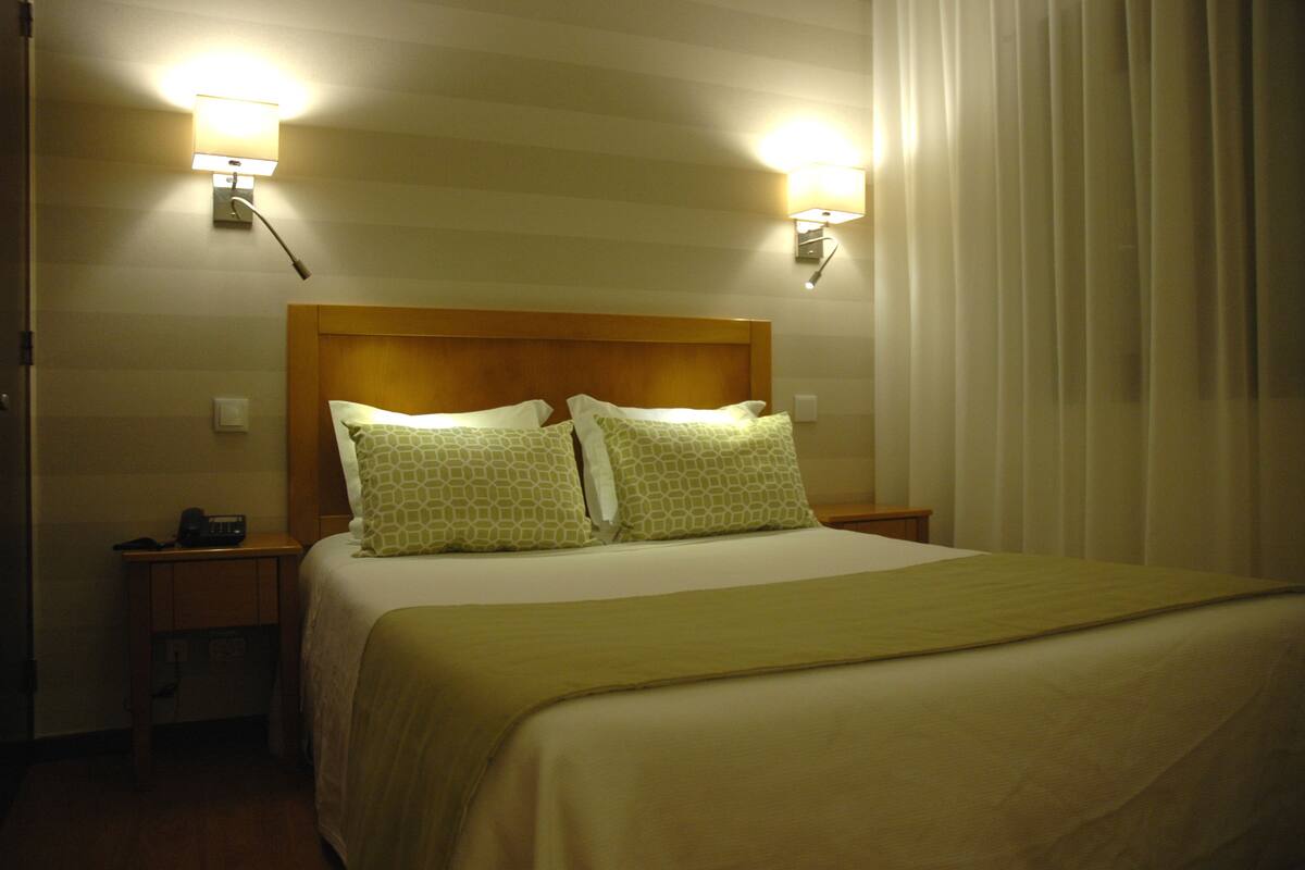 Una habitación de hotel con una cama grande, dos lámparas de noche, un cabecero de madera y una mesita de noche con un radio.