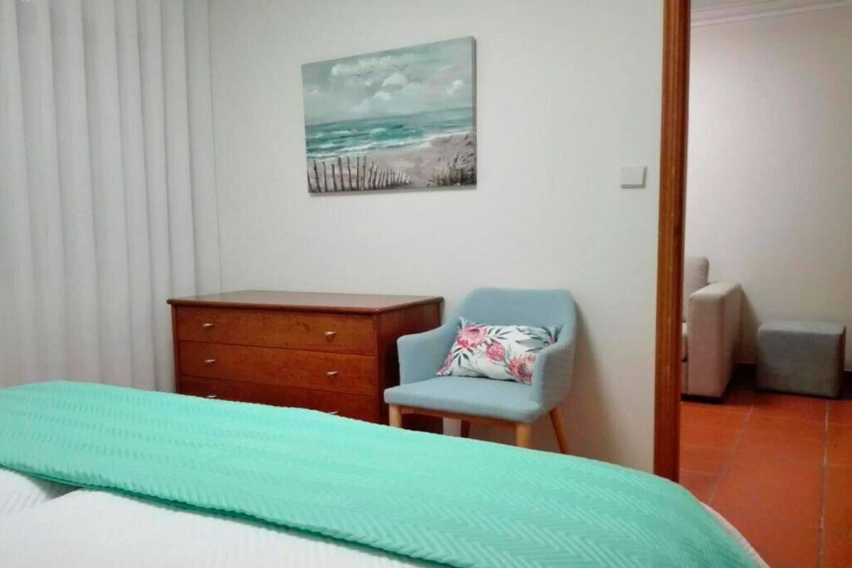 Un dormitorio con una cama, un aparador de madera, una silla y un cuadro de una playa.