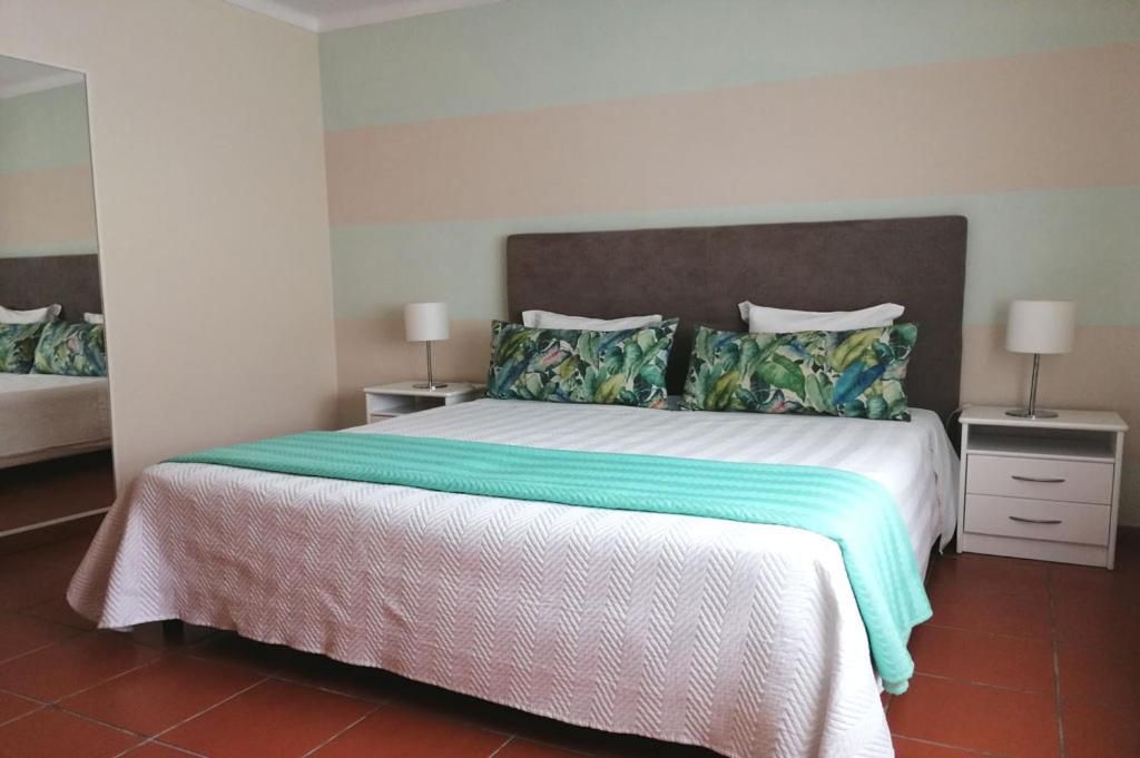 A neatly made bed with a white and green bedspread, two matching pillows, and a nightstand with a lamp.
