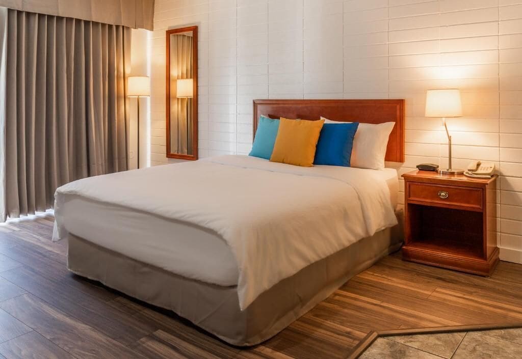 A hotel room with a large bed, a nightstand with a lamp, and a mirror on the wall.