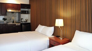 Habitación de hotel con dos camas, un panel de pared de madera, una kitchenette y una mesita de noche con lámpara.