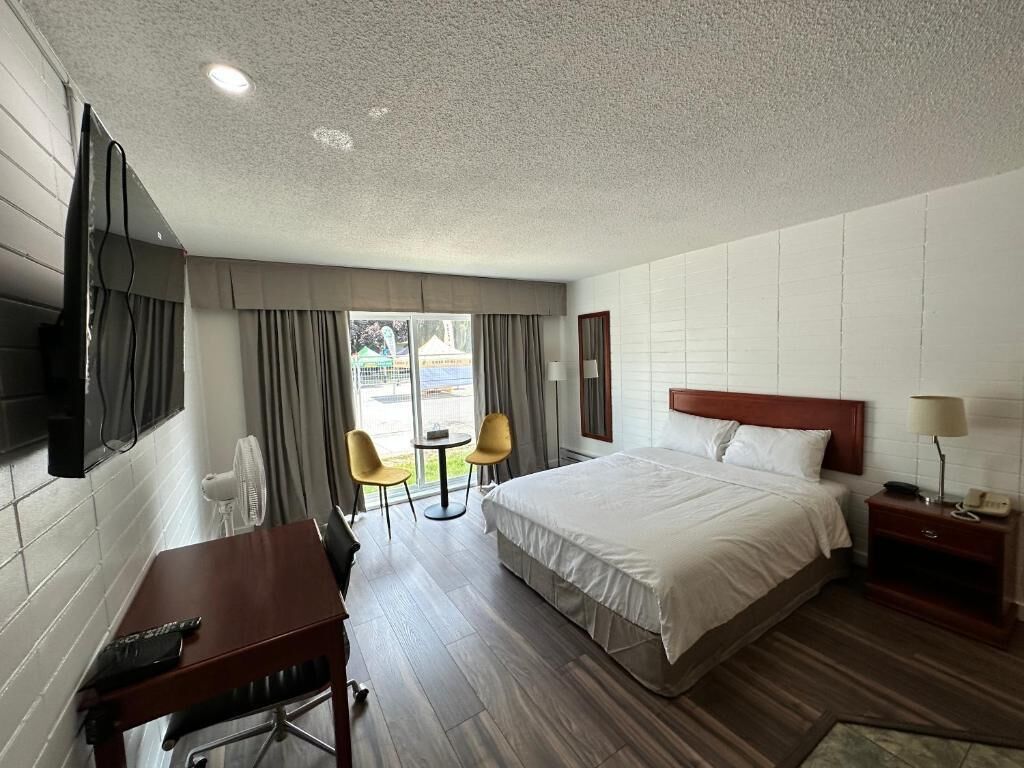 Habitación de hotel con cama, escritorio, silla, televisor y ventana con cortinas.