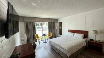 Habitación de hotel con cama, escritorio, silla, televisor y ventana con cortinas.