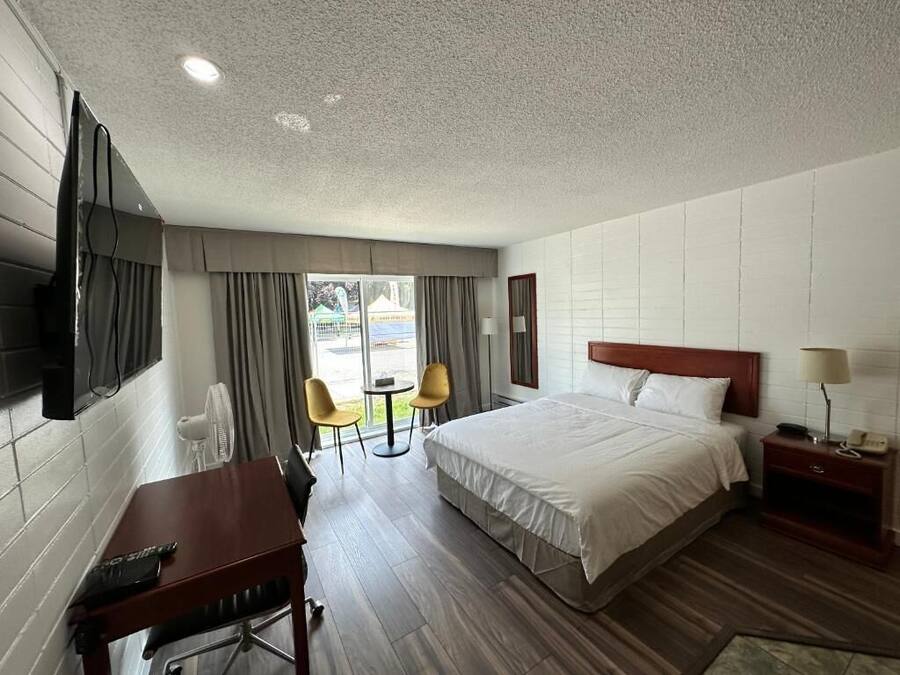 Habitación de hotel con cama, escritorio, silla, televisor y ventana con cortinas.