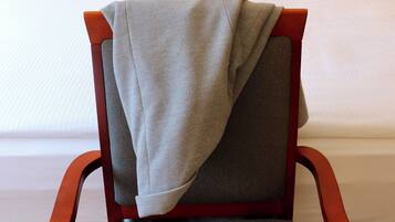 A hotel room with a bed, a chair with a blanket, a book, and a cup on a table.