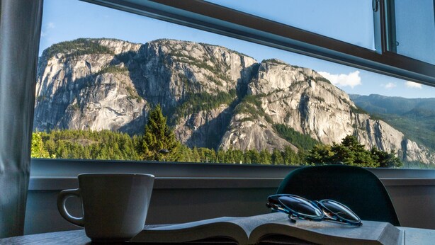 Una ventana con vistas a un paisaje montañoso, una taza y un libro abierto sobre una mesa.