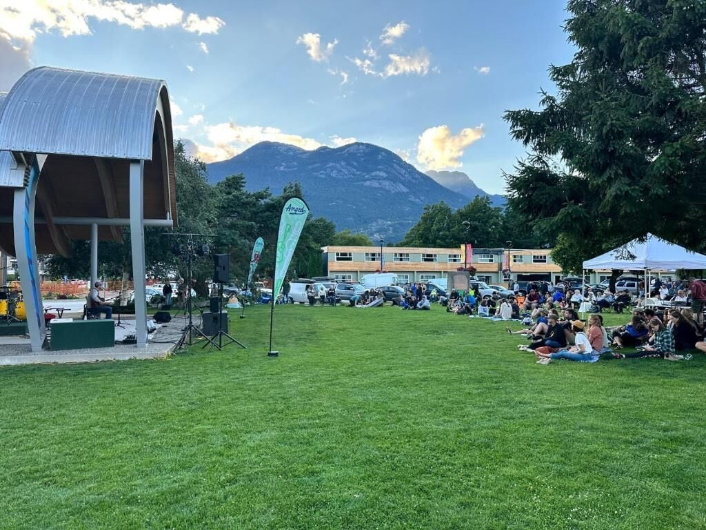 An outdoor event with a stage, audience, and buildings in the background.