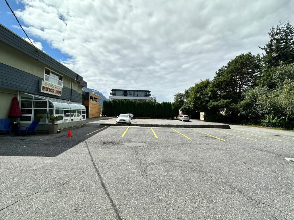 Un parking avec un bâtiment portant l’inscription « MOTOR INN » sur le côté gauche, une voiture blanche garée sur le parking et un grand arbre sur le côté droit.