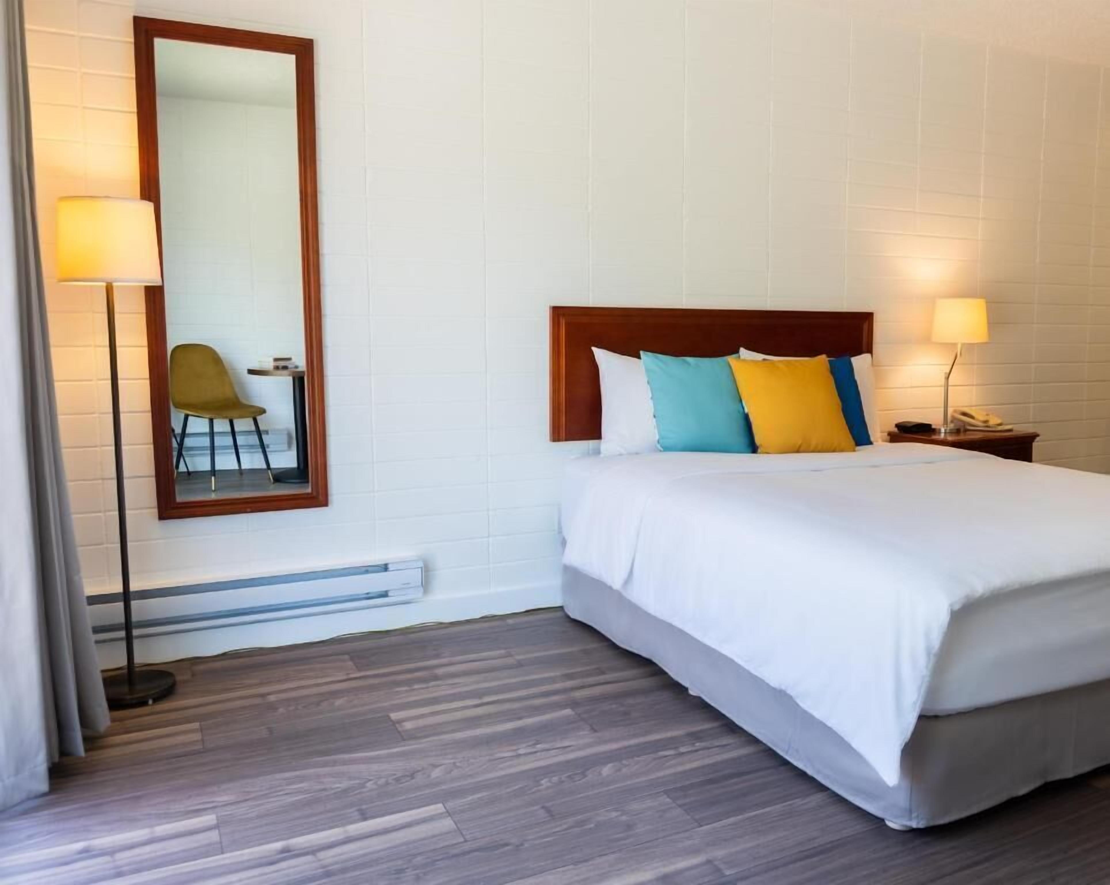 A hotel room with a bed, bedside lamps, a mirror, and a chair.