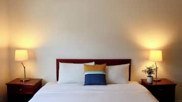 Una cama bien hecha con sábanas blancas, un cabecero de madera y dos mesitas de noche con lámparas.