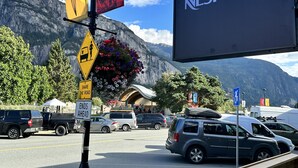Un estacionamiento con un cartel de Nespresso, un asta con banderas y montañas al fondo.