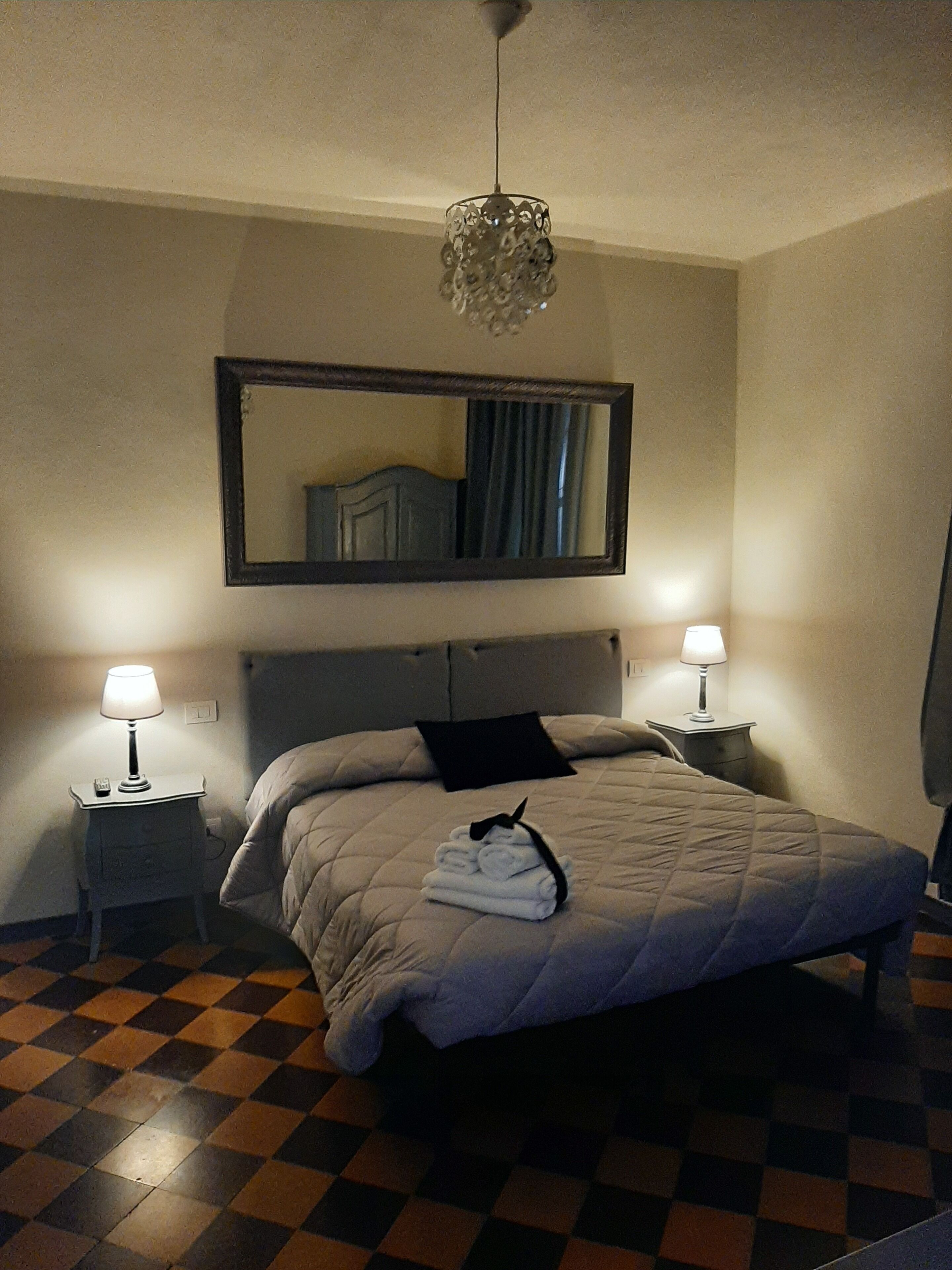 A hotel room with a bed, two bedside tables with lamps, a large mirror, and a checkered floor.