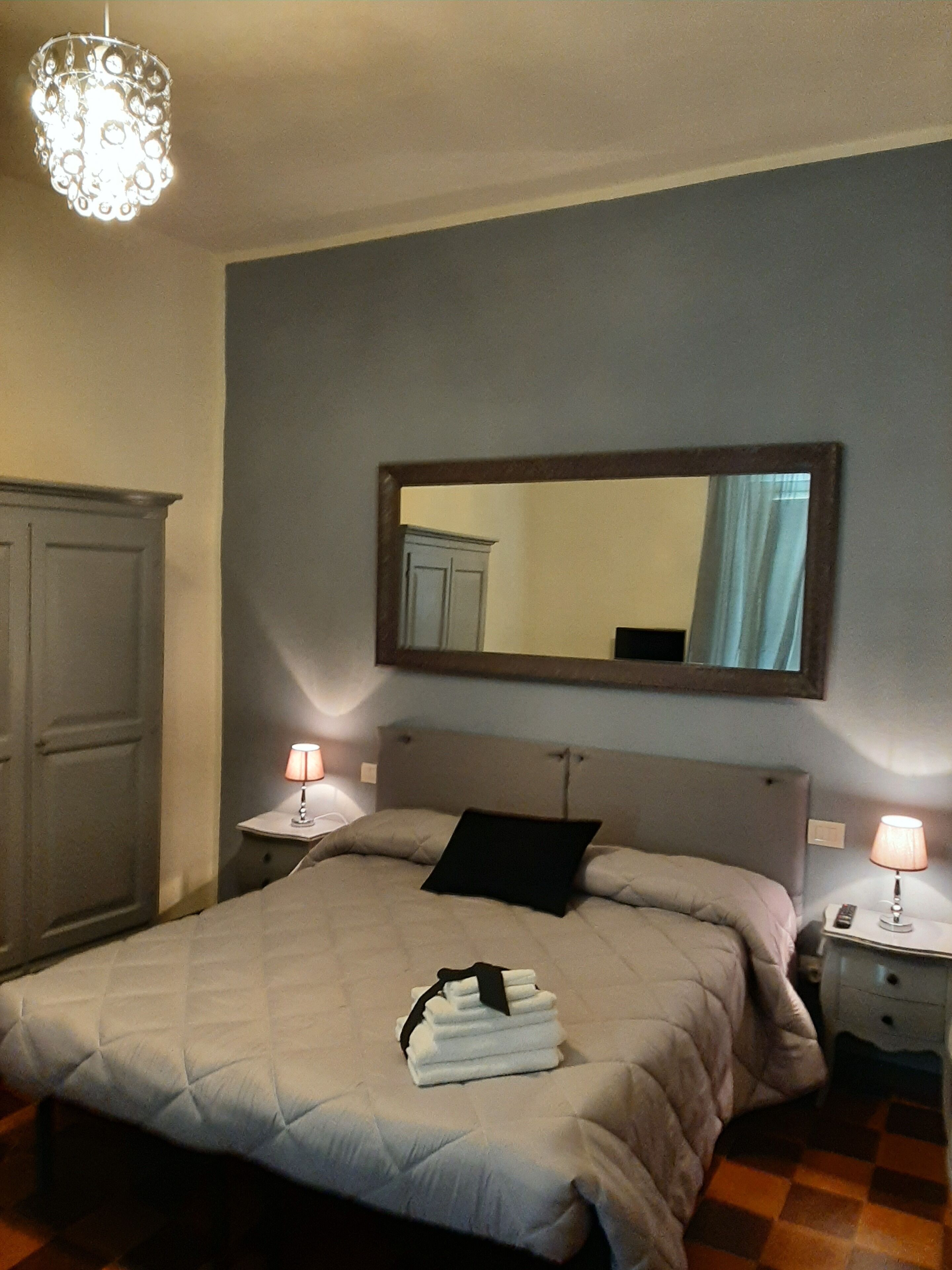 Un dormitorio con una cama, dos mesitas de noche con lámparas, un espejo y un armario.
