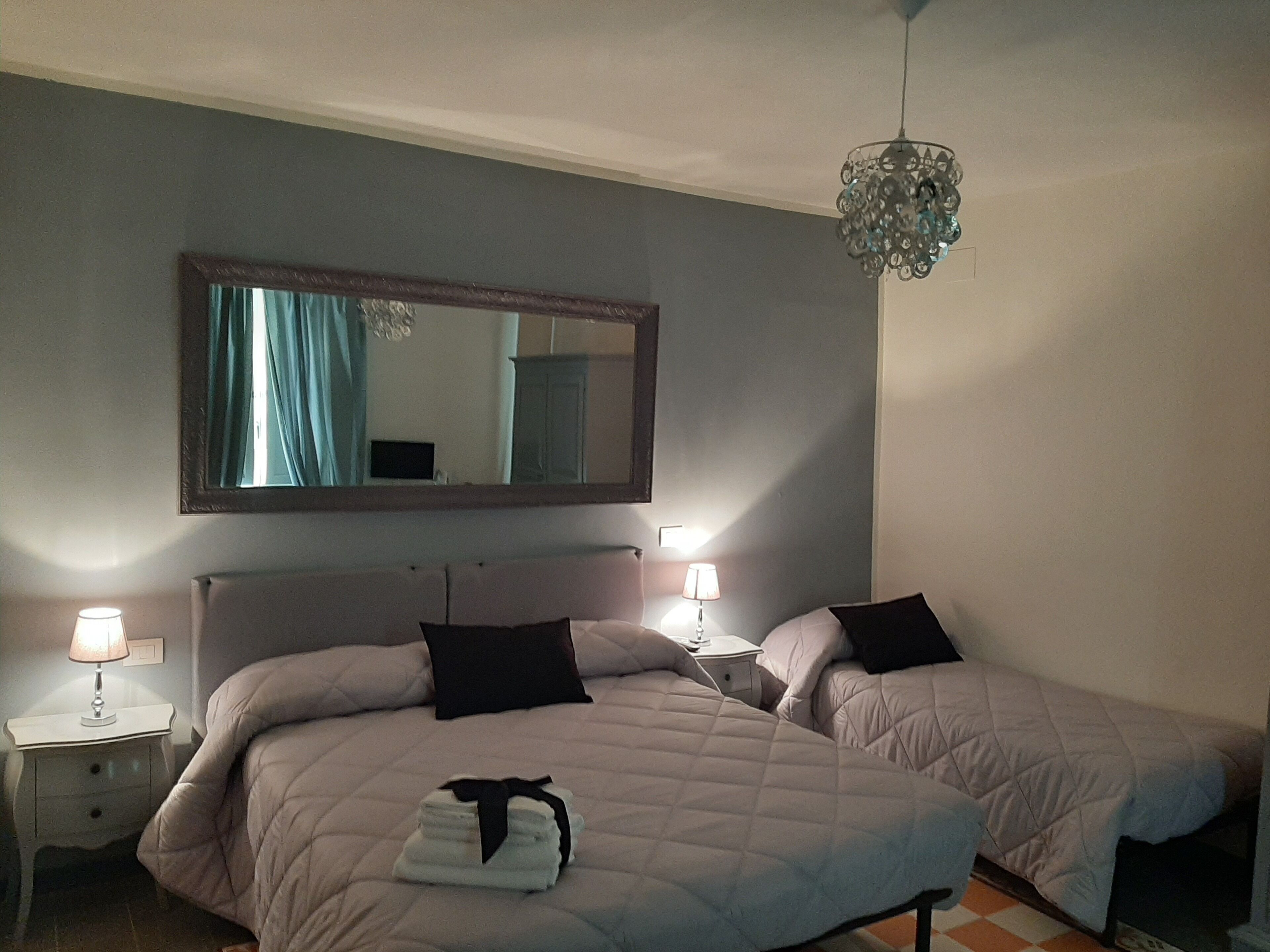 A hotel room with two beds, a large mirror, bedside lamps, and a chandelier.