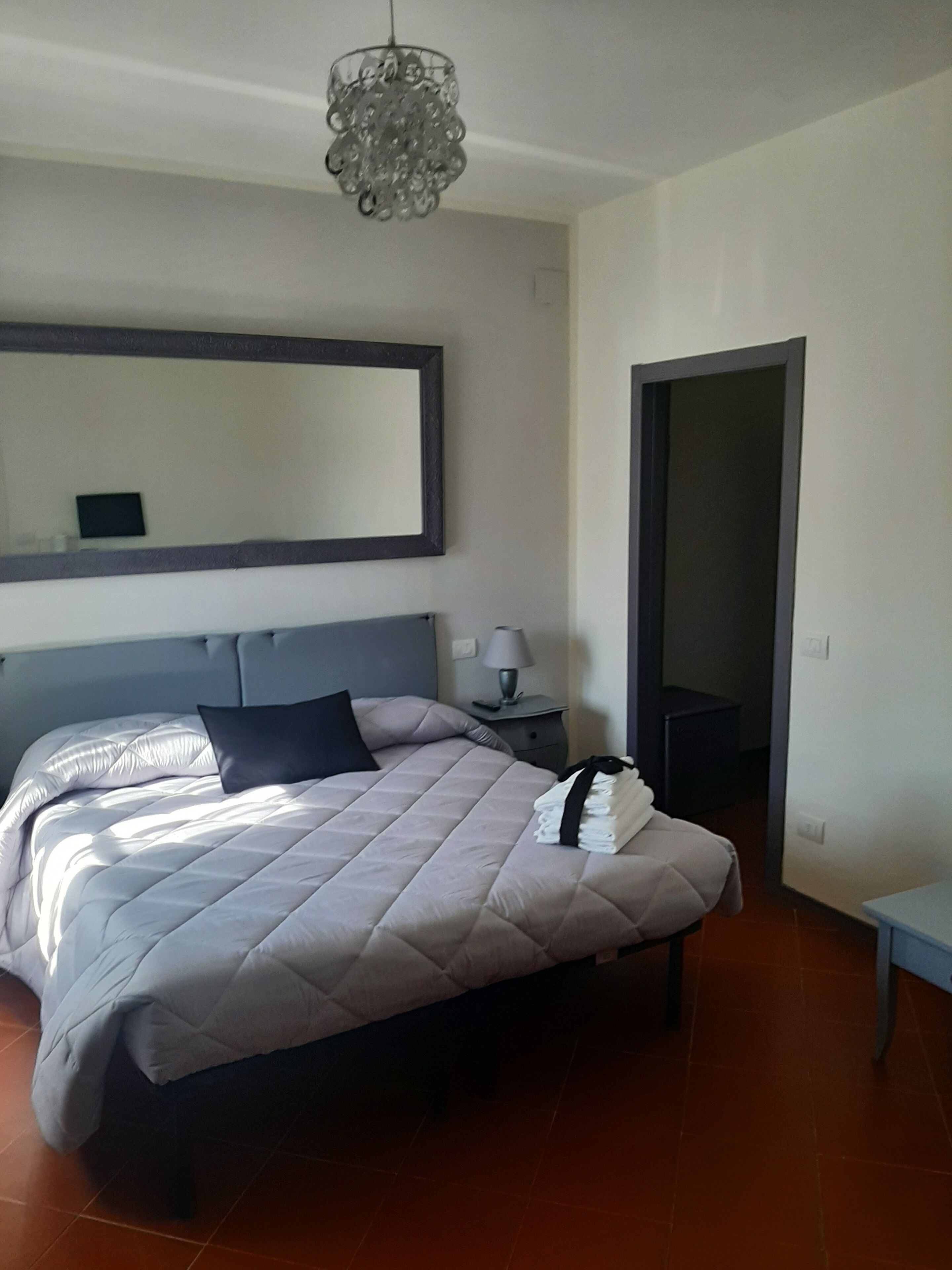 Un dormitorio moderno con una cama grande, una mesita de noche, una lámpara y un espejo.