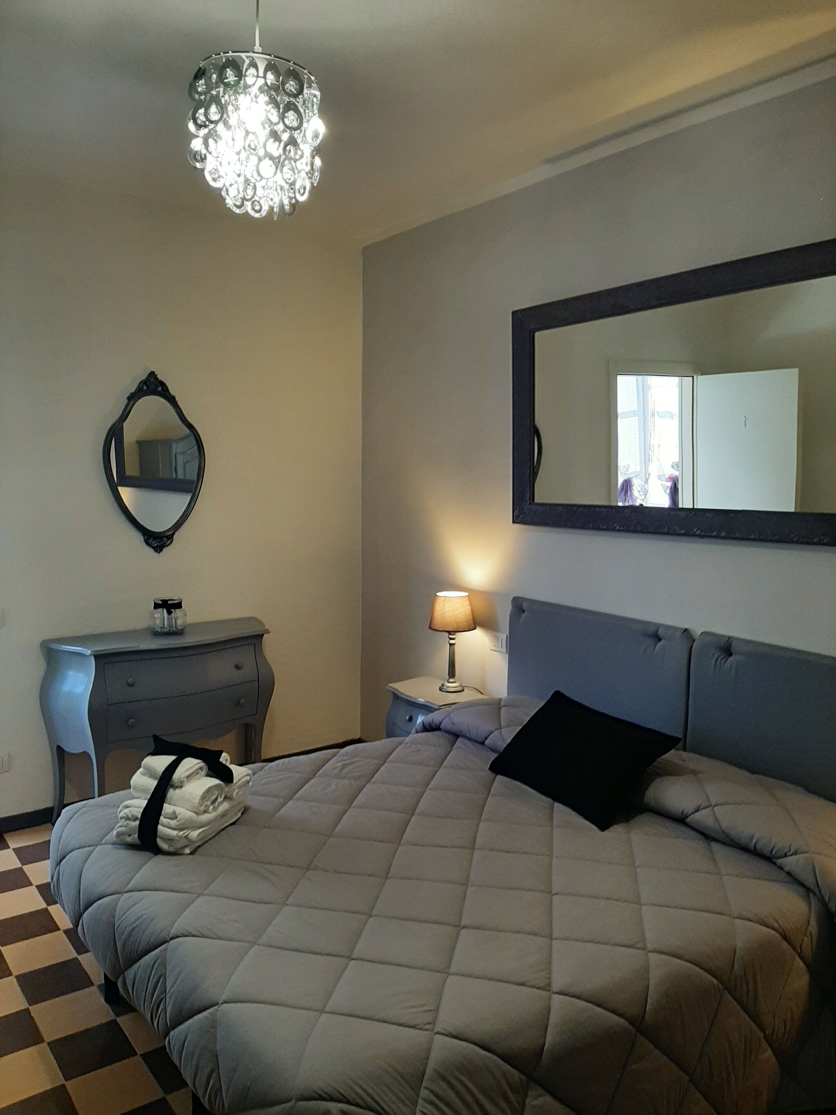 Een slaapkamer met een bed, een kaptafel, een nachtkastje met lamp, een spiegel en een kroonluchter.