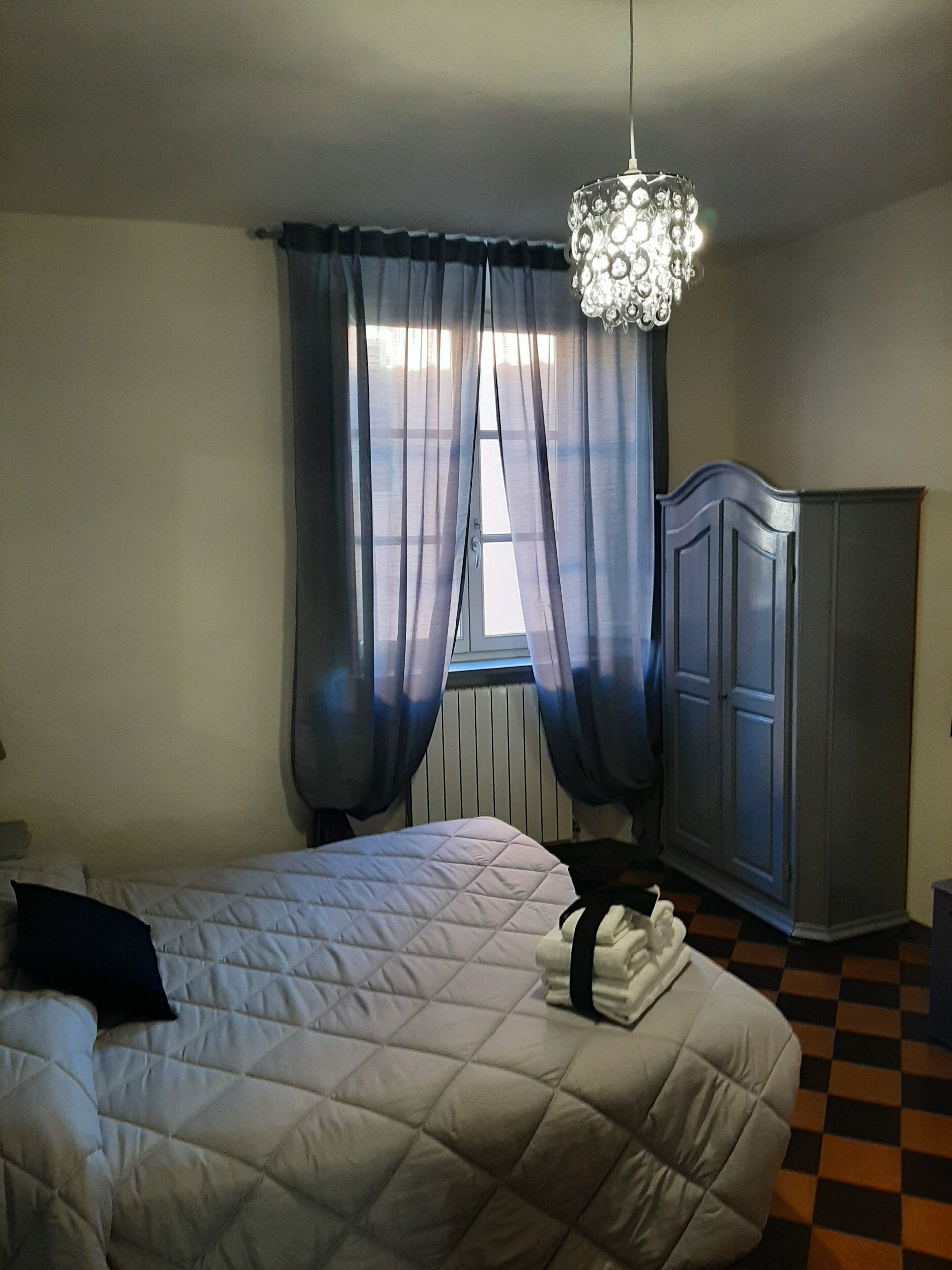 Une chambre à coucher avec un lit, une armoire, un lustre et des rideaux en voile.