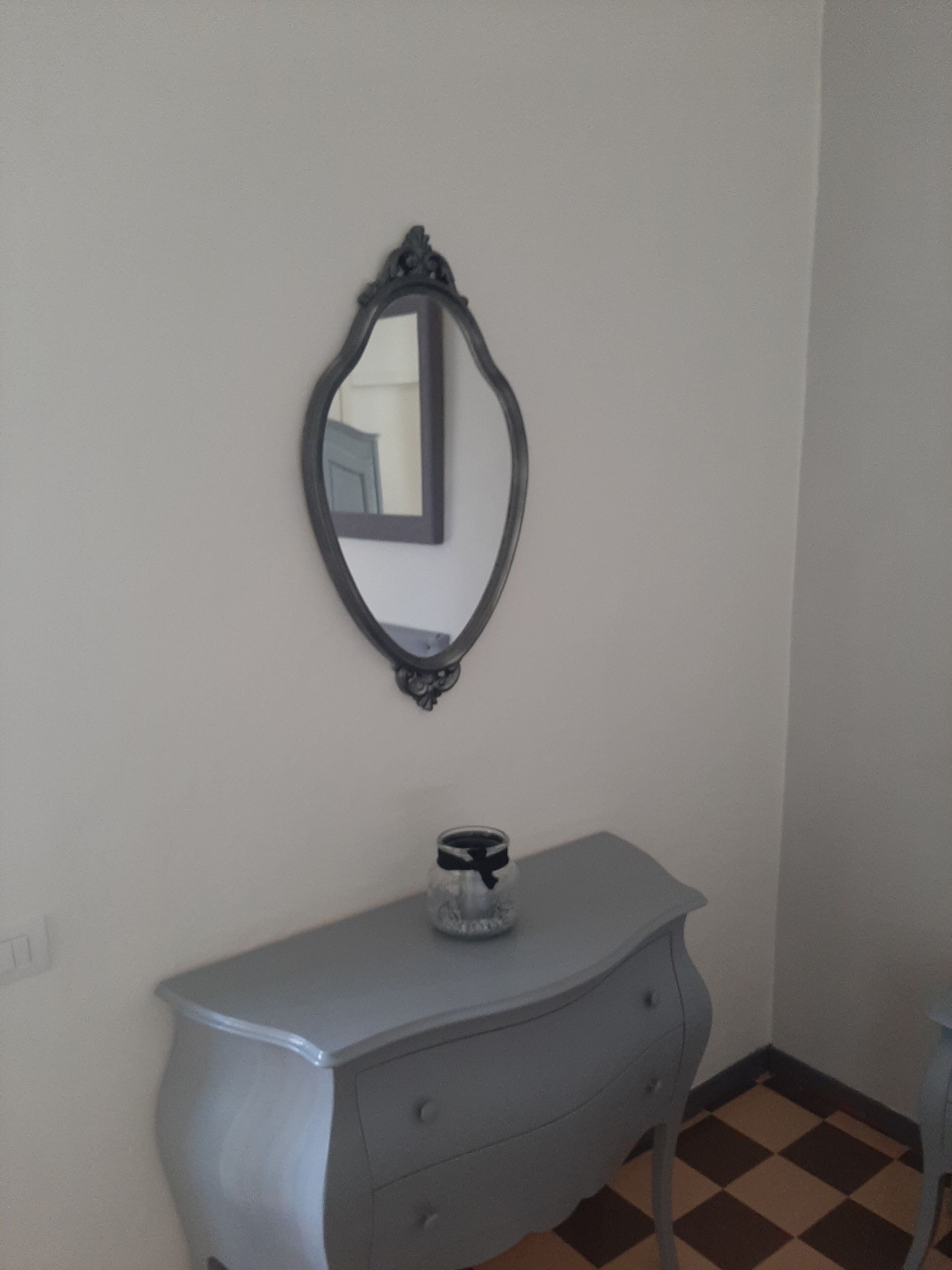 Eine Ecke eines Raumes mit einem Wandspiegel, einem kleinen Tisch mit einer Glaseinlage und einem karierten Boden.