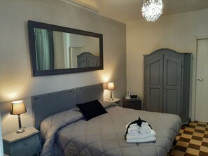 Un lit bien fait, avec un oreiller noir, deux lampes de chevet, un miroir au-dessus du lit et un sol à carreaux.