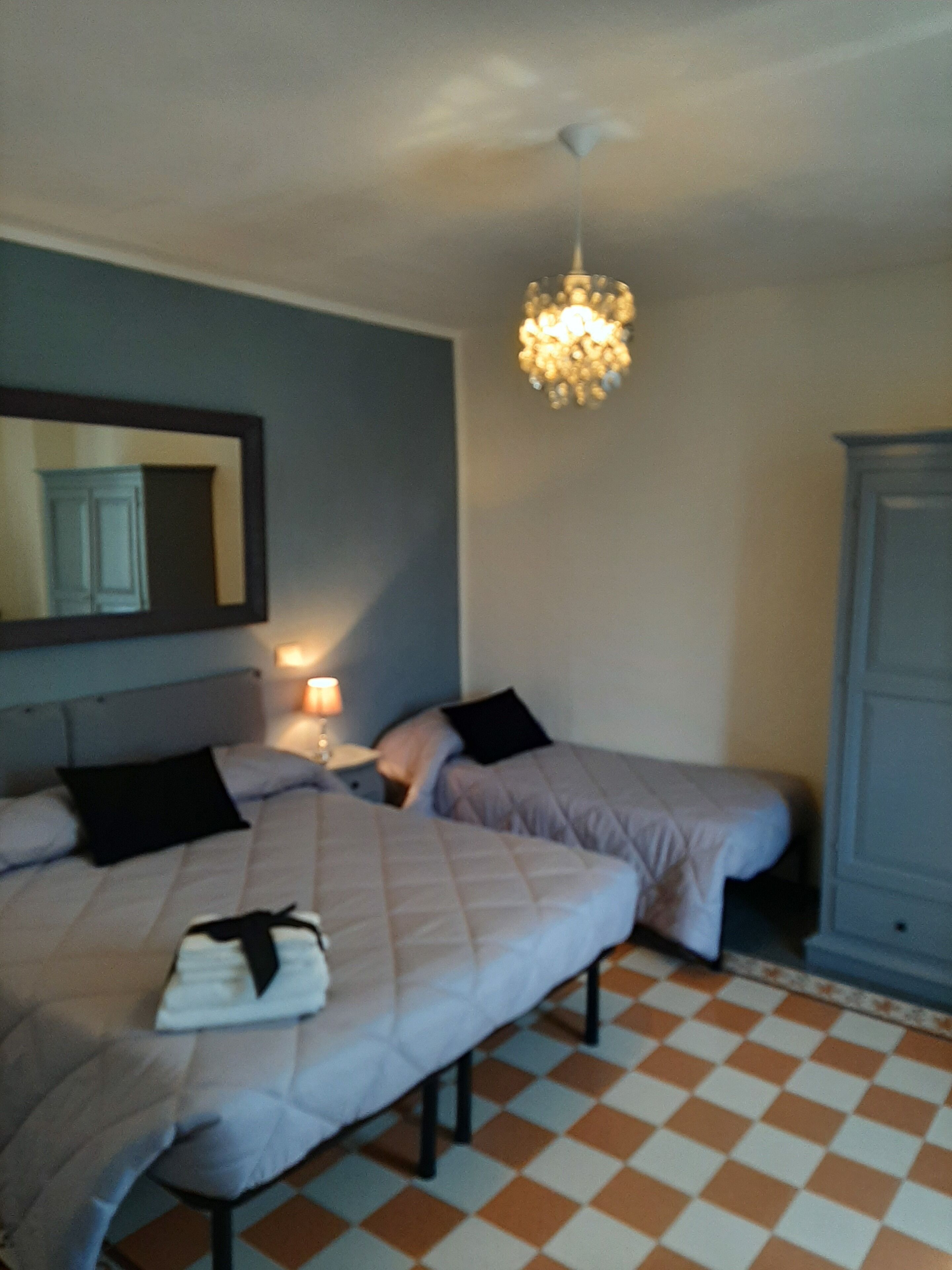 Una camera da letto con due letti, un comodino, una lampada, un lampadario, un armadio e un pavimento a scacchi.