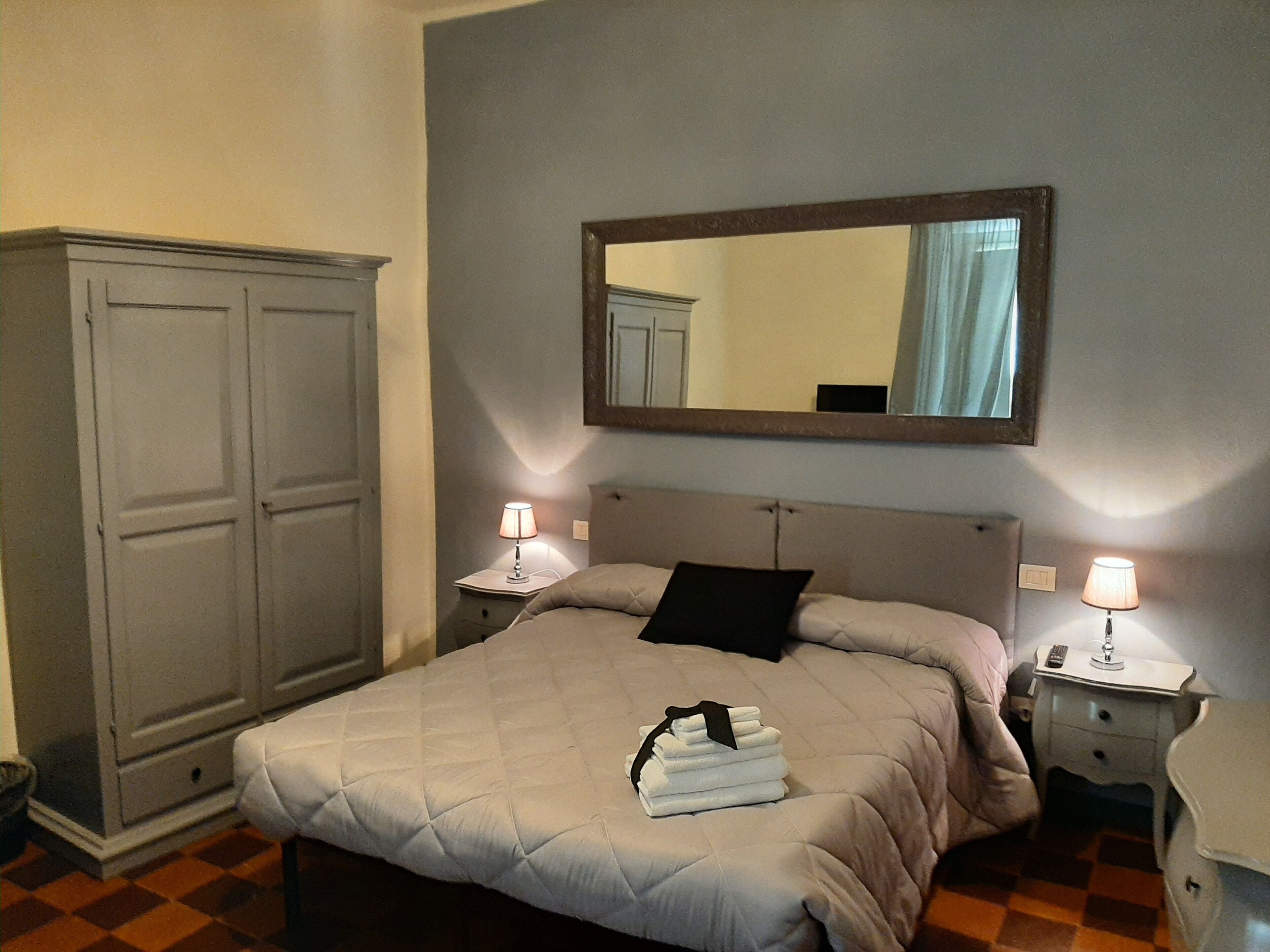 Una camera d'hotel con un letto, due comodini con lampade, un armadio e uno specchio a parete.