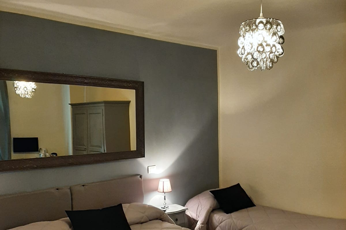 Quarto de hotel com duas camas, um espelho grande, um candelabro e um chão quadriculado.