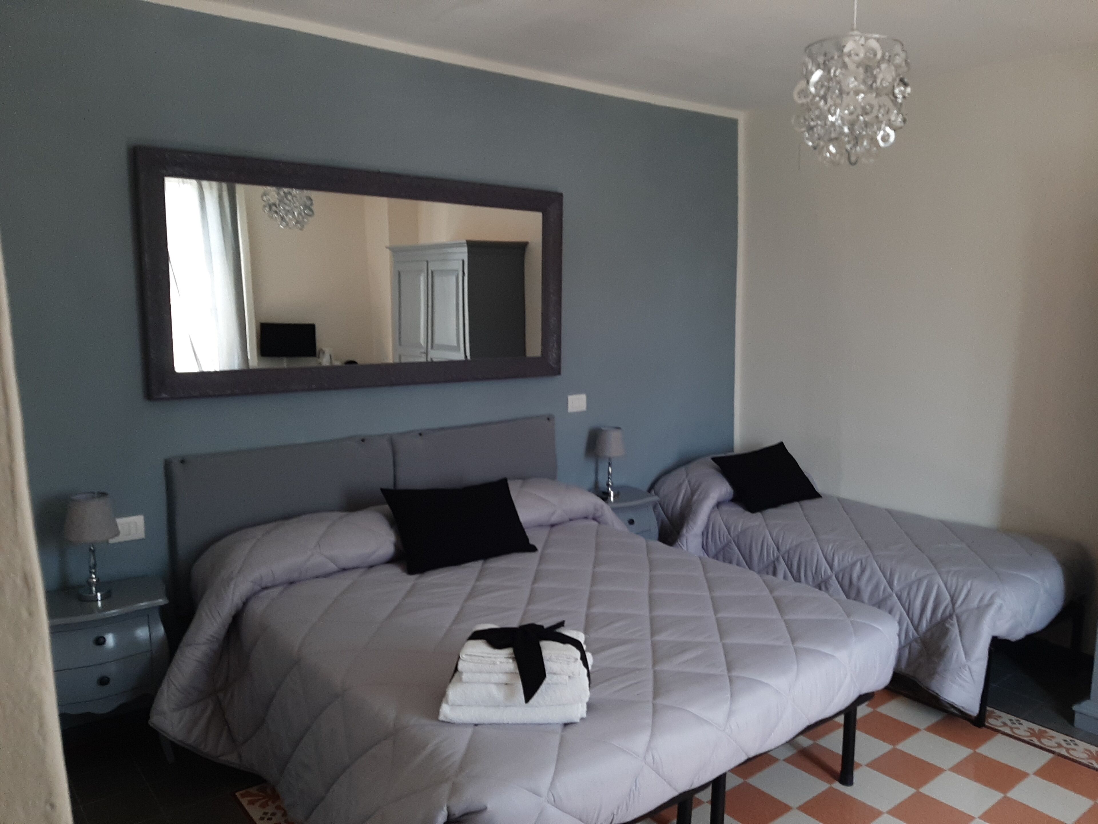 A bedroom with two beds, a large mirror, bedside lamps, and a chandelier.