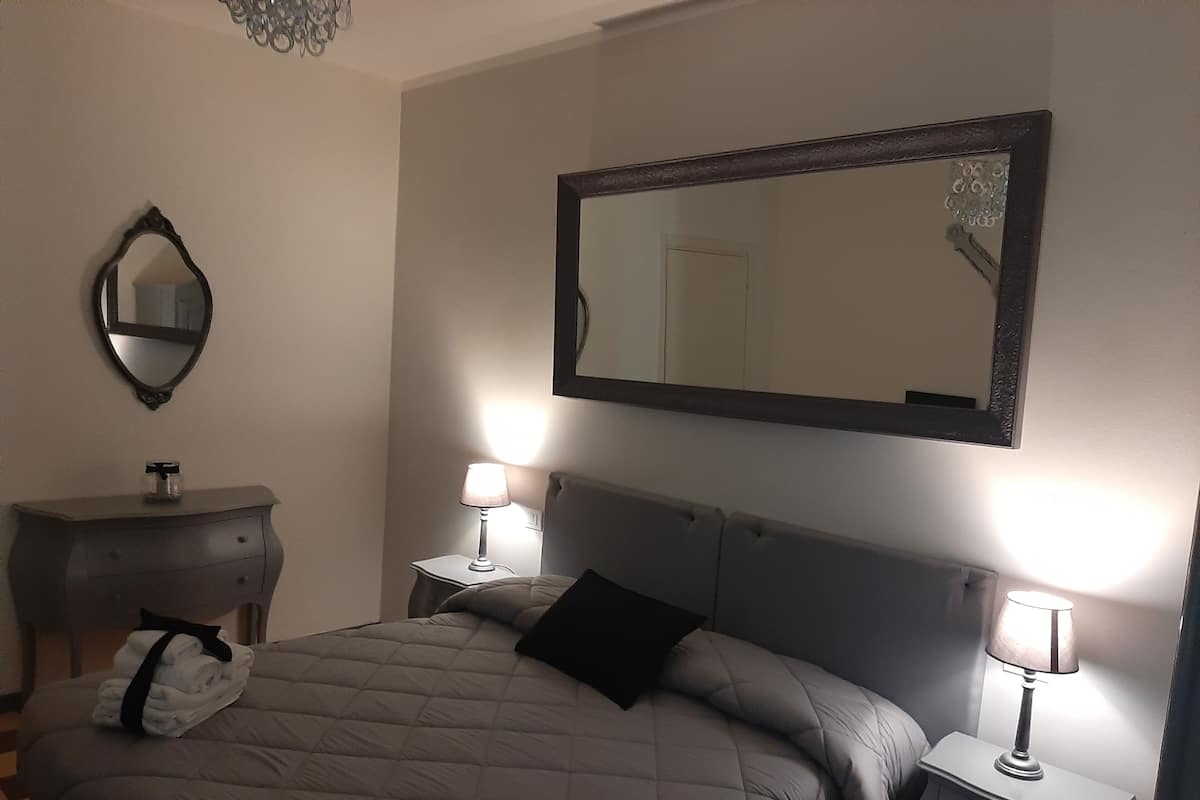 Quarto com uma cama, duas mesas de cabeceira com abajures, um penteado e um espelho na parede.