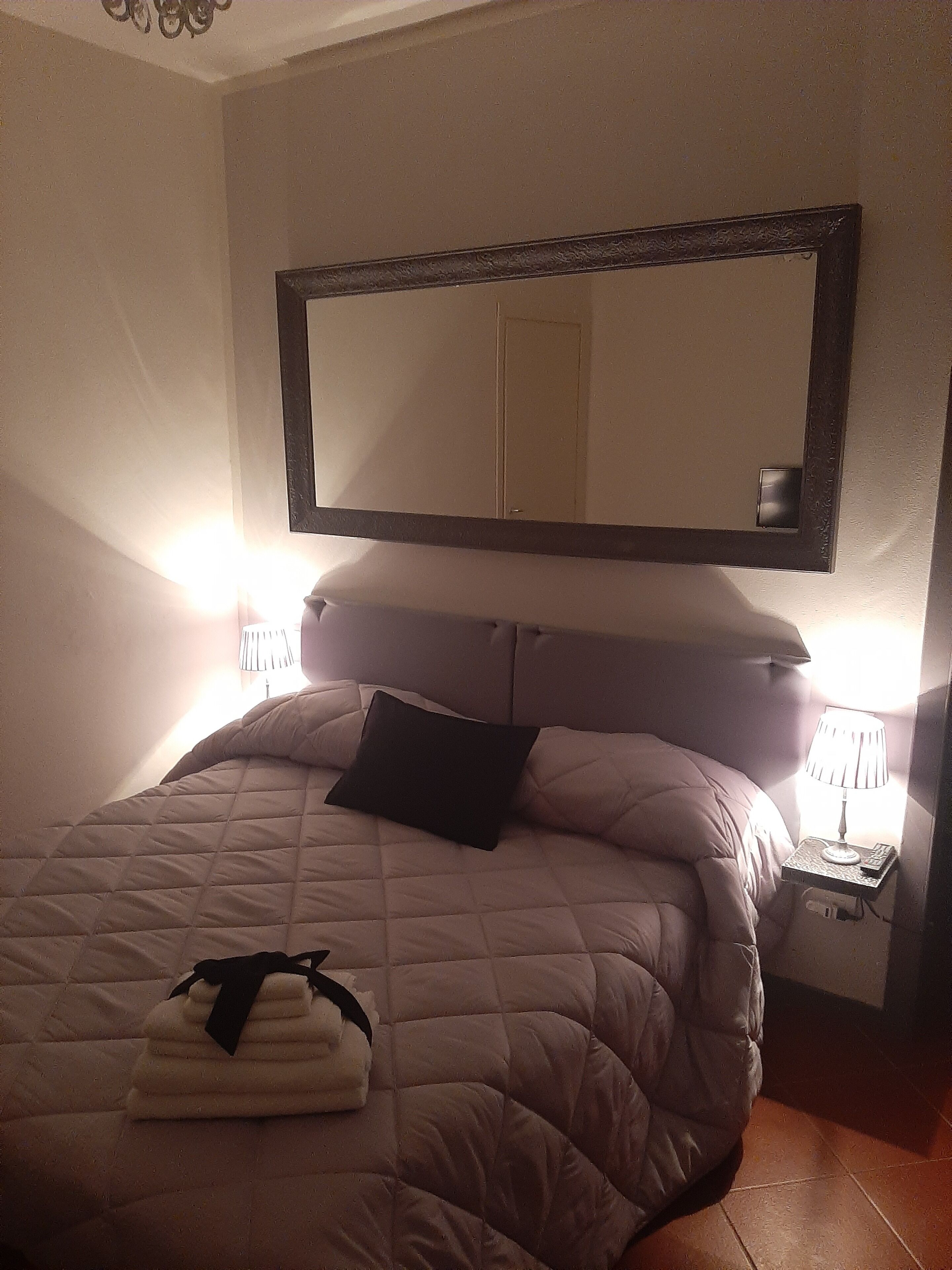 Ein Schlafzimmer mit einem großen Bett, einem Kopfteil, einem Nachttisch mit Lampe und einem Spiegel an der Wand.