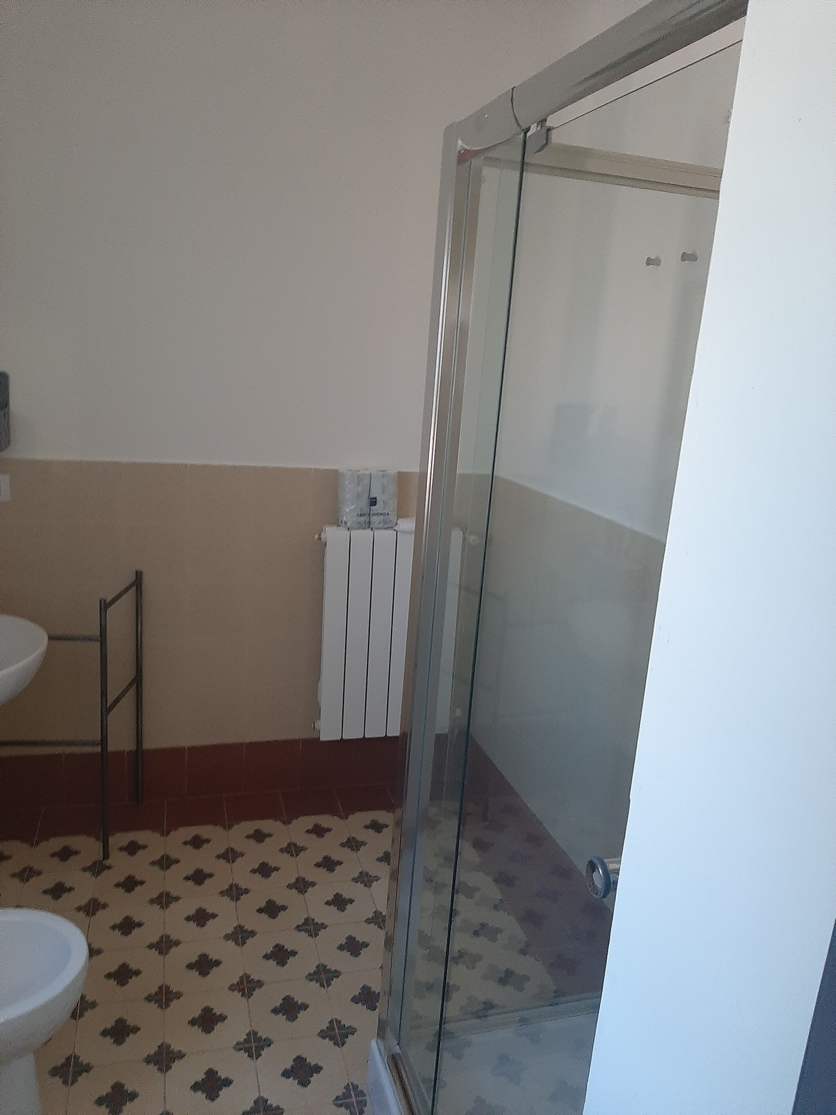 A bathroom with a toilet, a sink, a shower with a glass door, and a radiator.