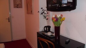 Een hotelkamer met een bureau, een stoel, een aan de muur bevestigde televisie, een vaas met bloemen en een deur.