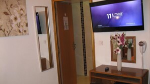 Hotelkamer met een televisie waarop een sportzender draait, een spiegel, een kleine koelkast en een telefoon.